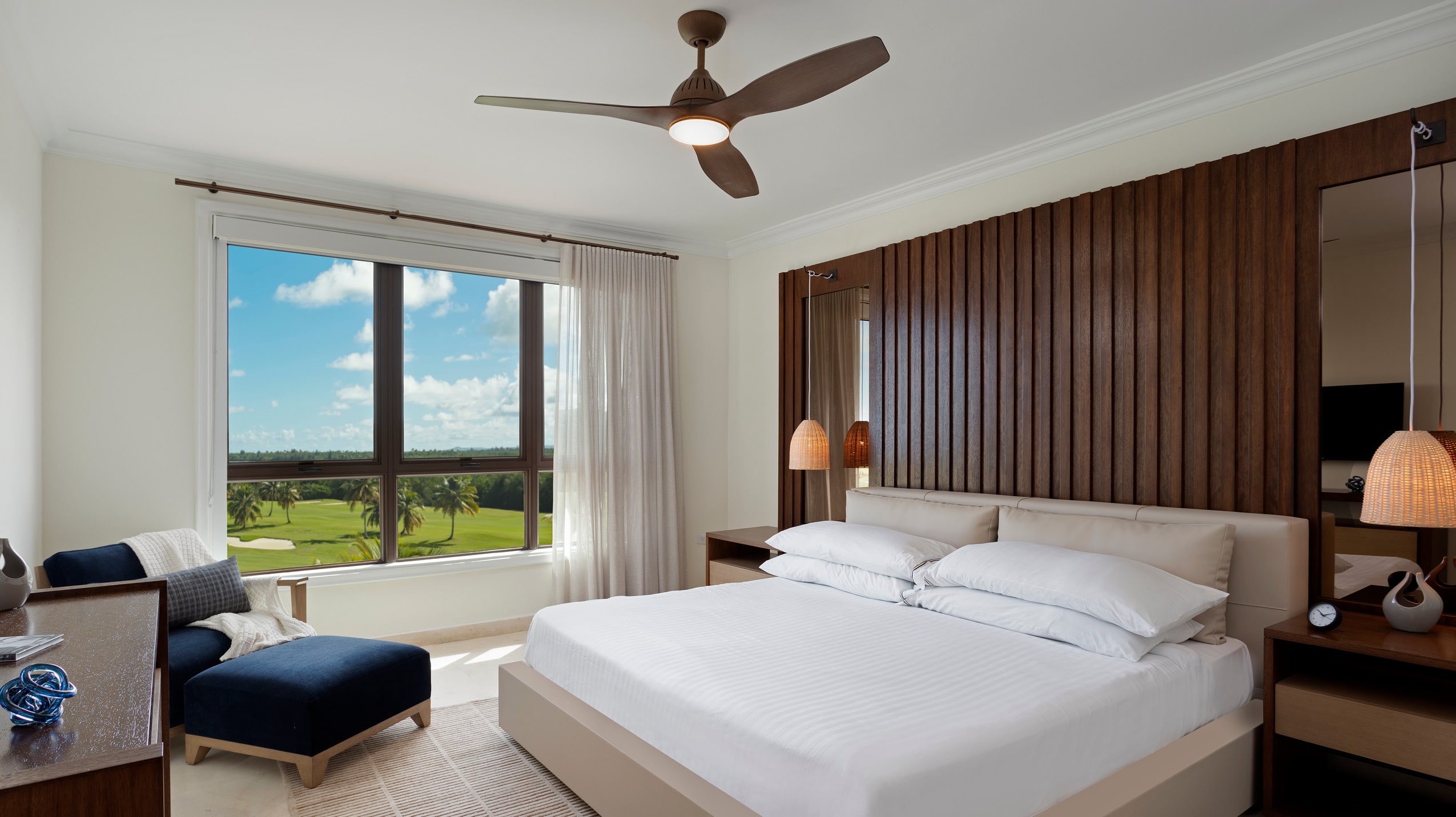 A well-appointed room at the Celeste Country Club Residences with a king-size bed, stylish furnishings, and a panoramic window offering views of the Grand Reserve golf course.