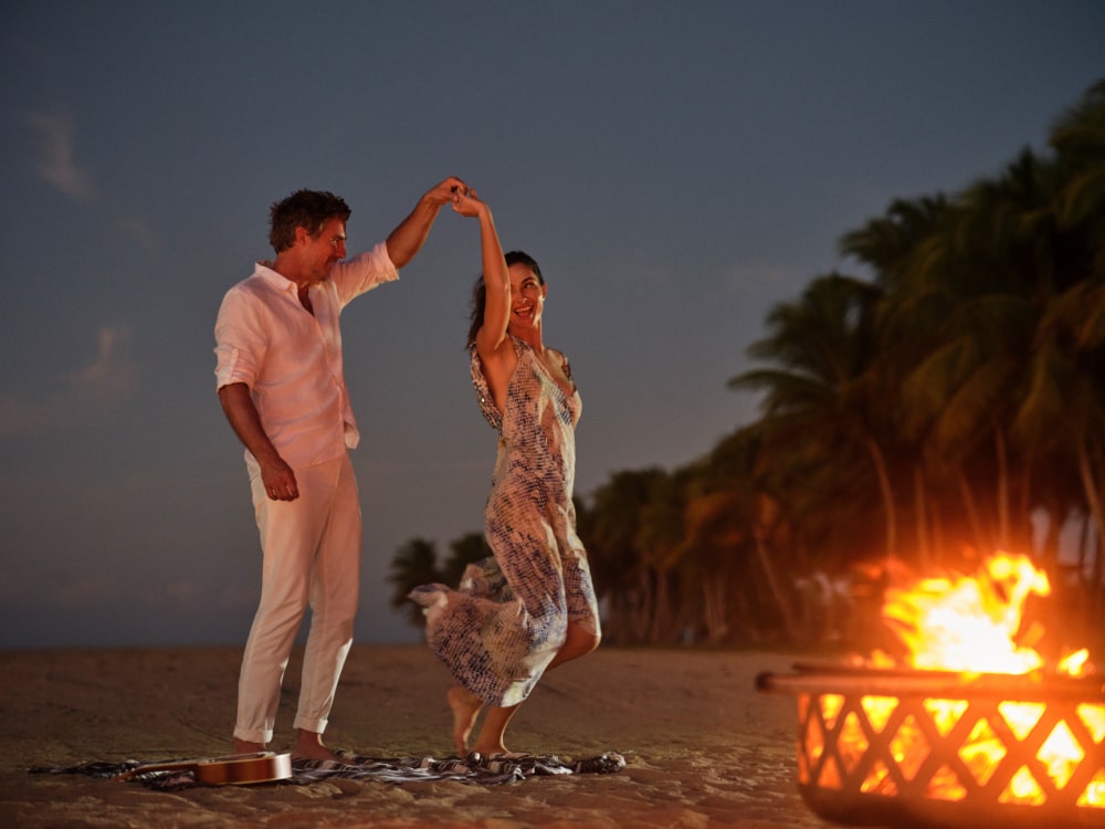 A couple dances on the beach at Grand Reserve, enveloped by the warmth of a beach bonfire and the enchantment of Puerto Rico's evenings