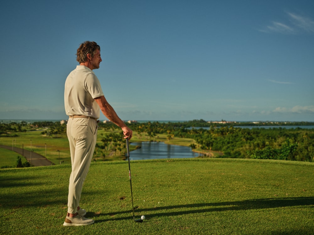 A golfer contemplating his next swing on the pristine golf course at Grand Reserve, with a panoramic view of Puerto Rico's natural beauty